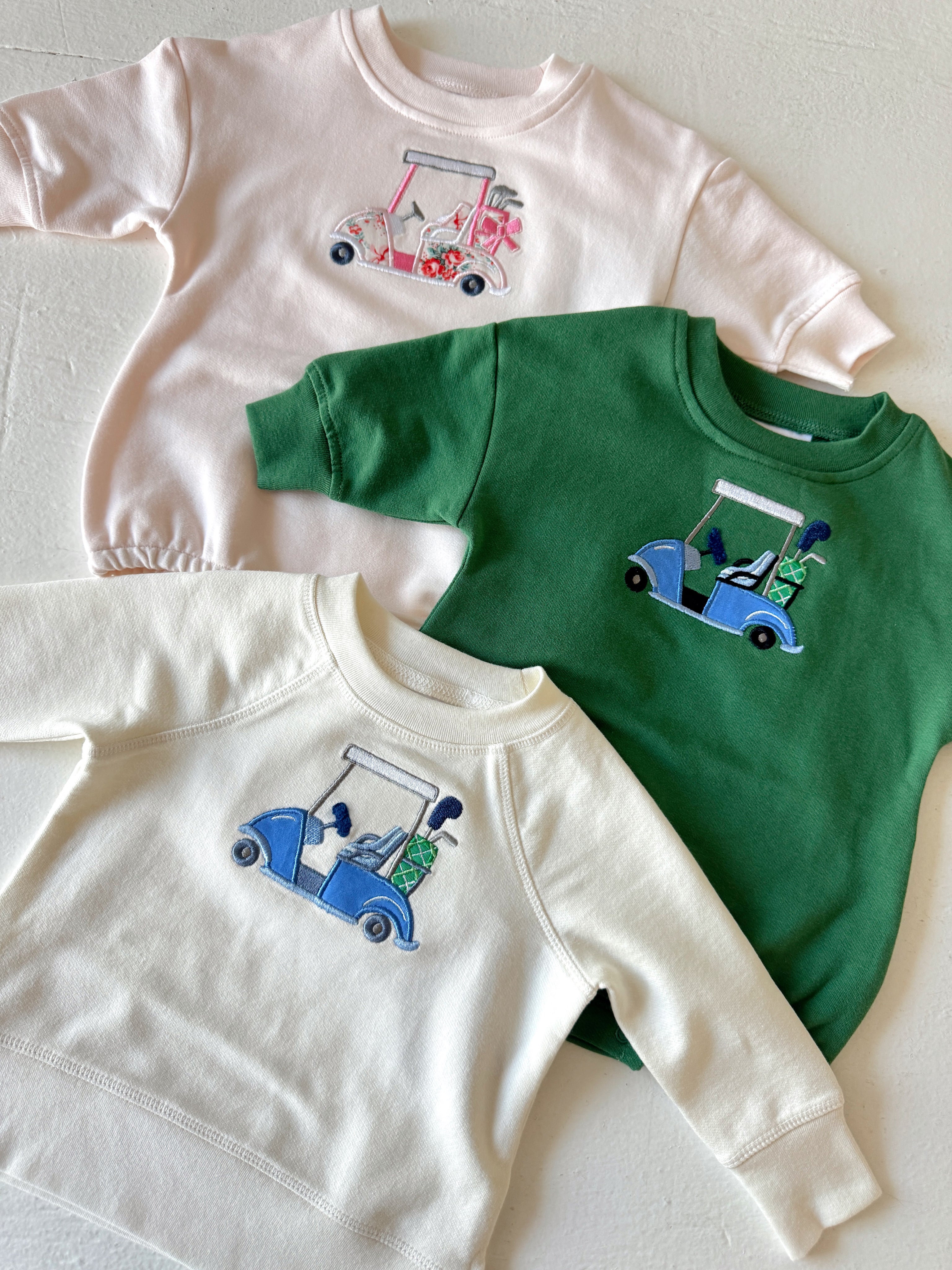 Three sweatshirts: pink, green, and white, each featuring a golf cart embroidery design.