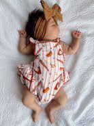 Baby girl sleeping on a white textured blanket, wearing a food-print romper and a large bow headband.