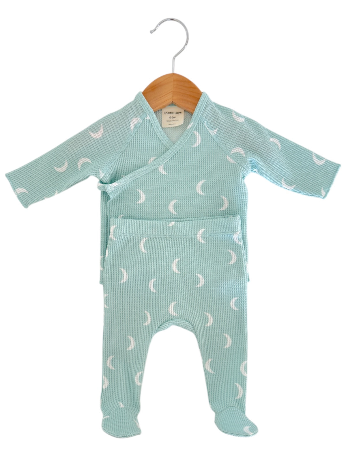 Light blue baby outfit with crescent moon pattern, hung on a wooden hanger.