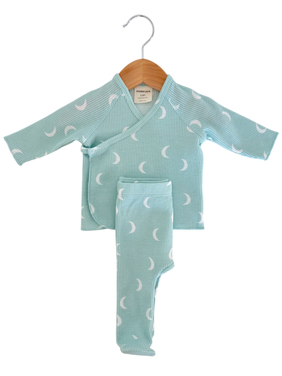 Mint green baby outfit with white crescent moon pattern hanging on a wooden hanger.