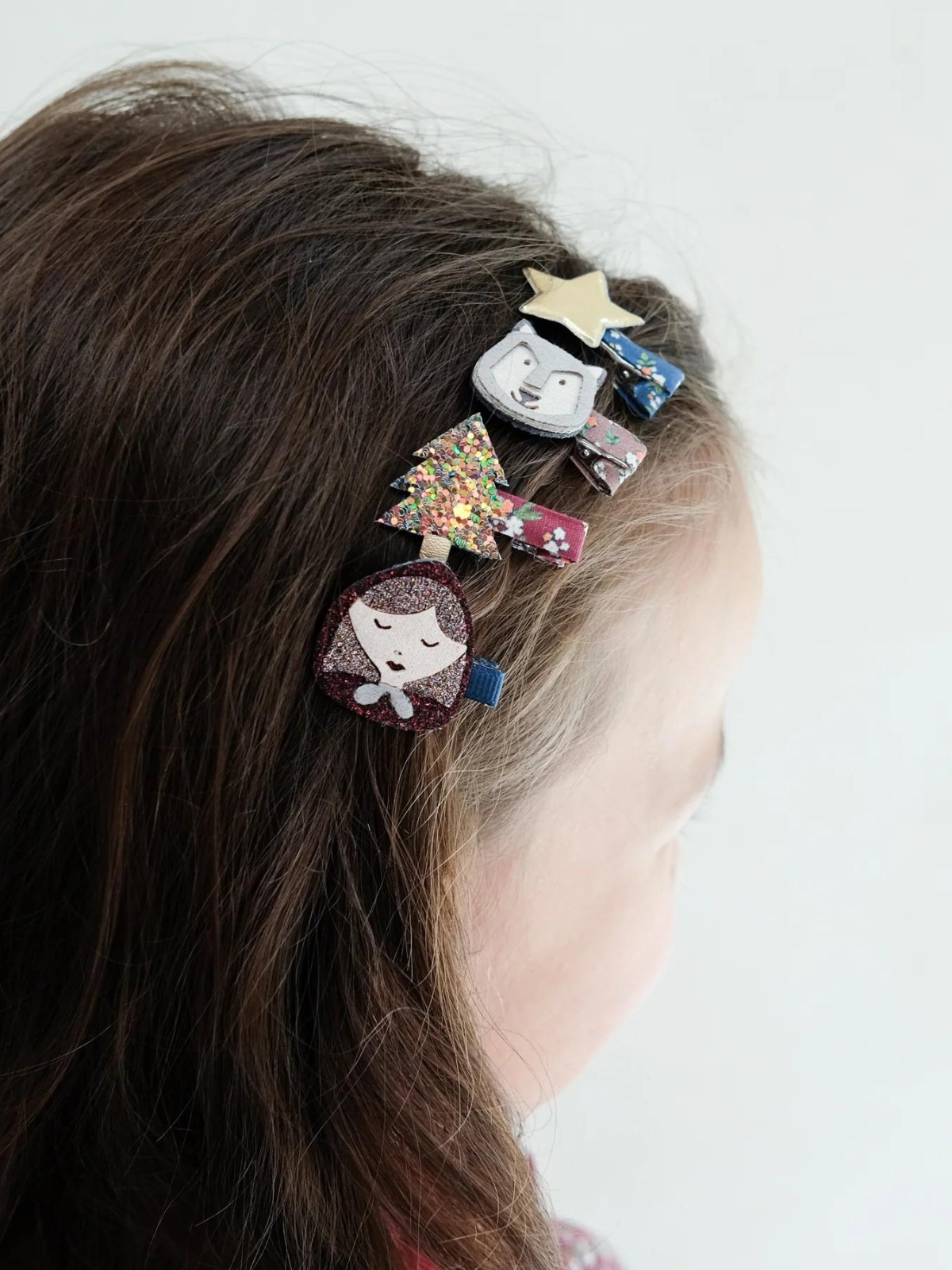 Colorful hair clips decorate a child's hair, featuring stars, trees, and whimsical characters.