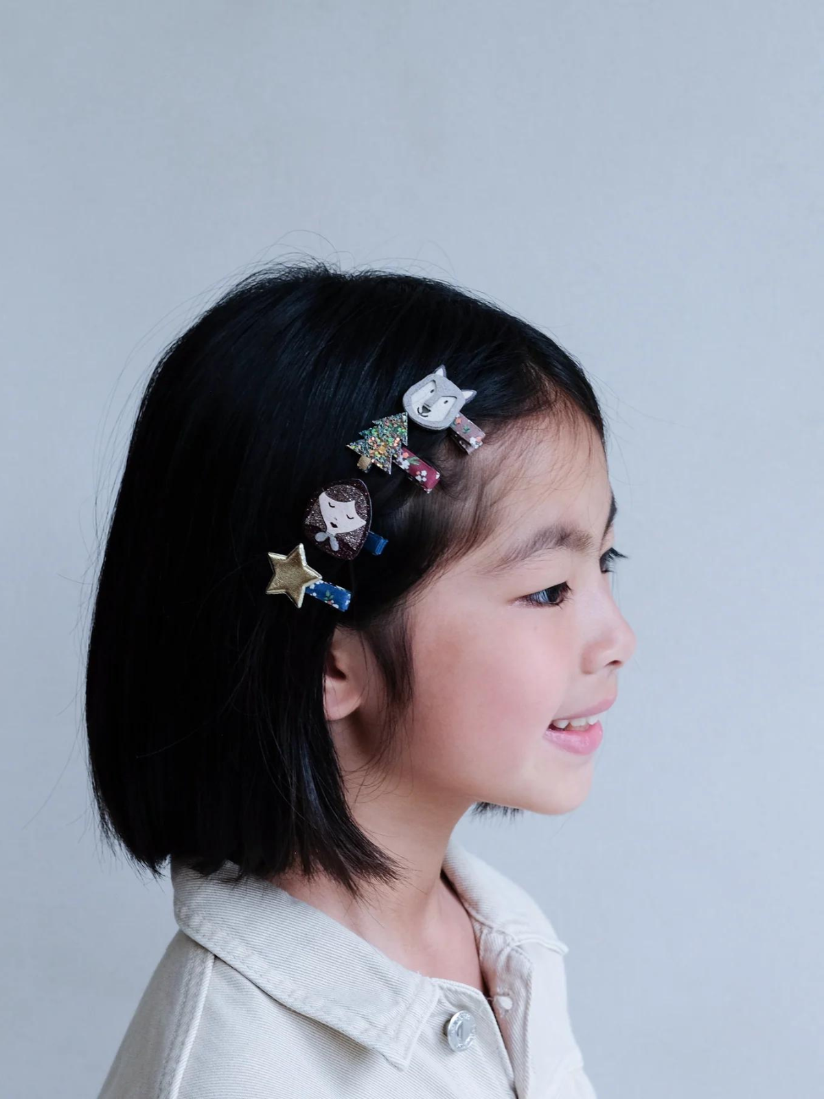 Child with bob haircut wearing colorful hair clips in a profile view against a light grey background.