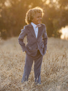Smiling child in a stylish suit standing in a sunlit field, exuding confidence and joy.