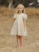 Girl in a polka dot dress standing barefoot in a dry field.