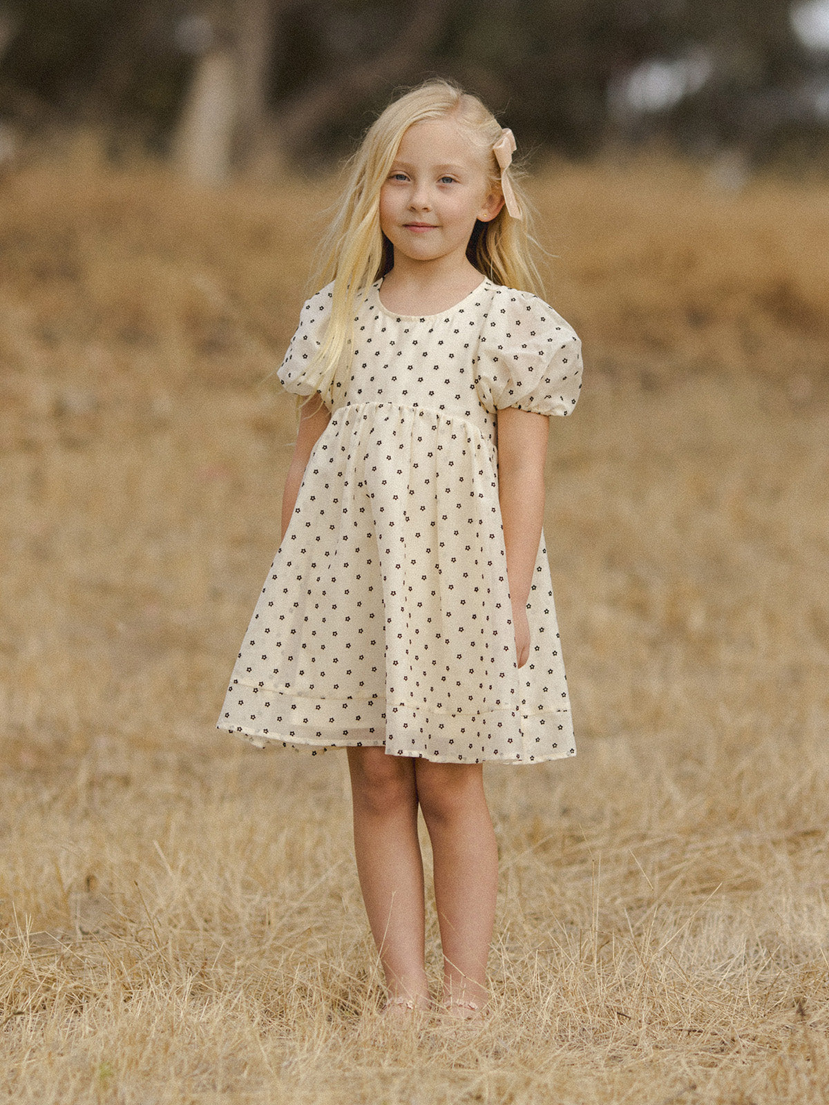 Girl in a polka dot dress standing barefoot in a dry field.