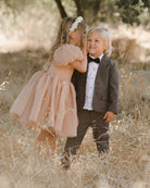 Two young children sharing a moment in a sunlit field, dressed elegantly for a special occasion.