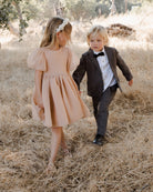 Two children walking in a field; a girl in a pink dress and a boy in a suit with a bow tie.