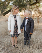 Two children holding hands in a field, wearing formal attire, smiling at each other.