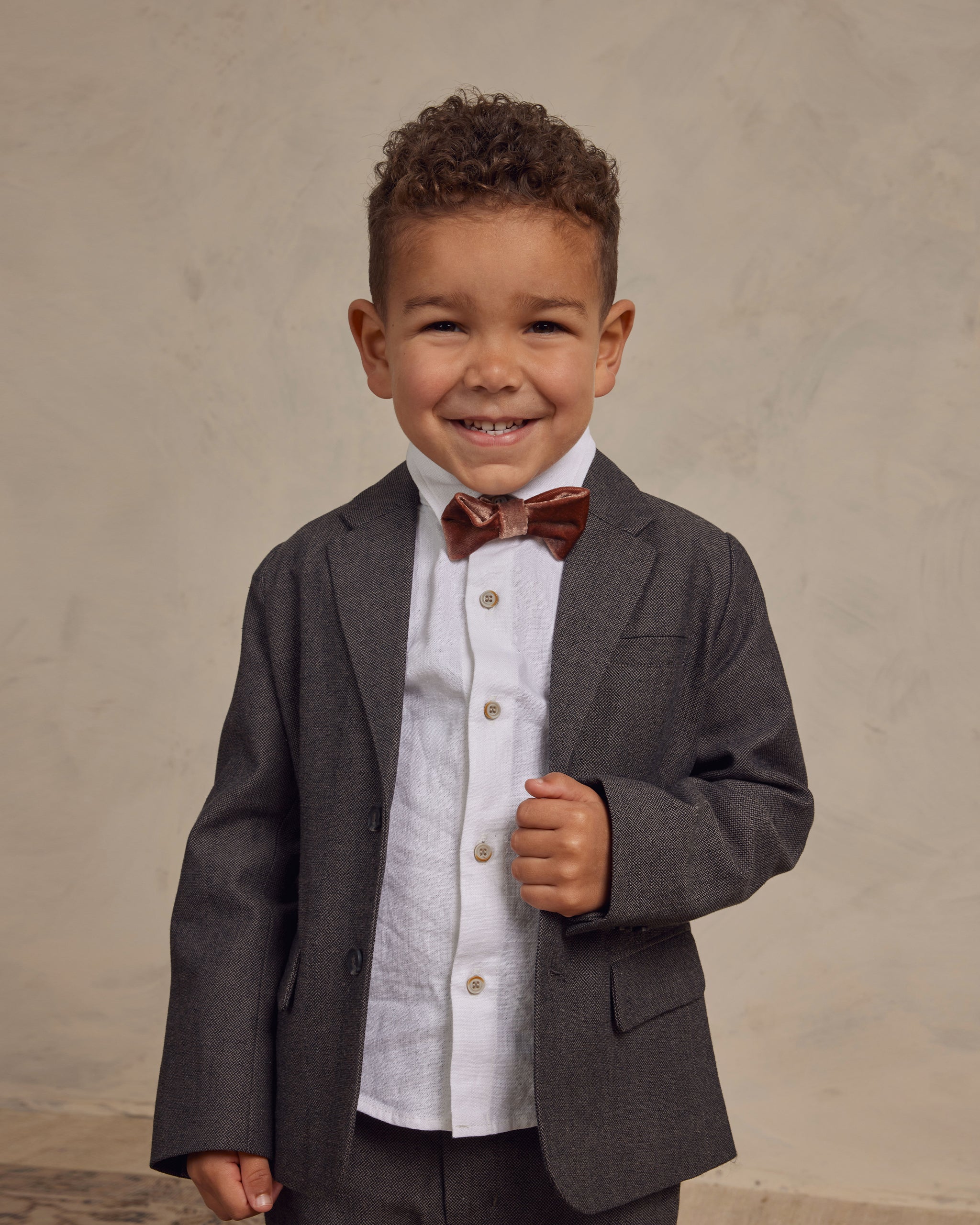 Smiling boy in a suit and bow tie, posing confidently against a neutral background.