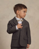 Young boy in a tailored gray suit and bow tie, looking thoughtfully to the side, with a neutral background.