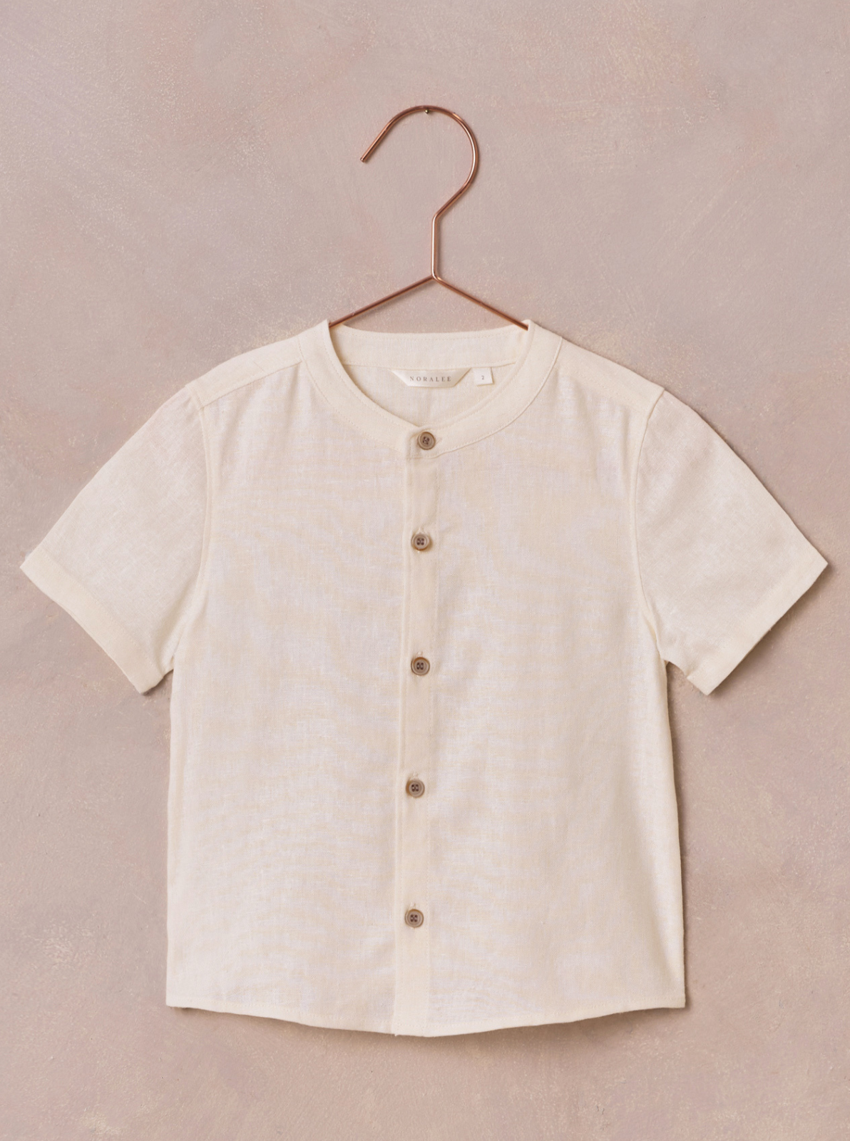 Light beige short-sleeve button-up shirt hanging on a copper hook against a textured background.