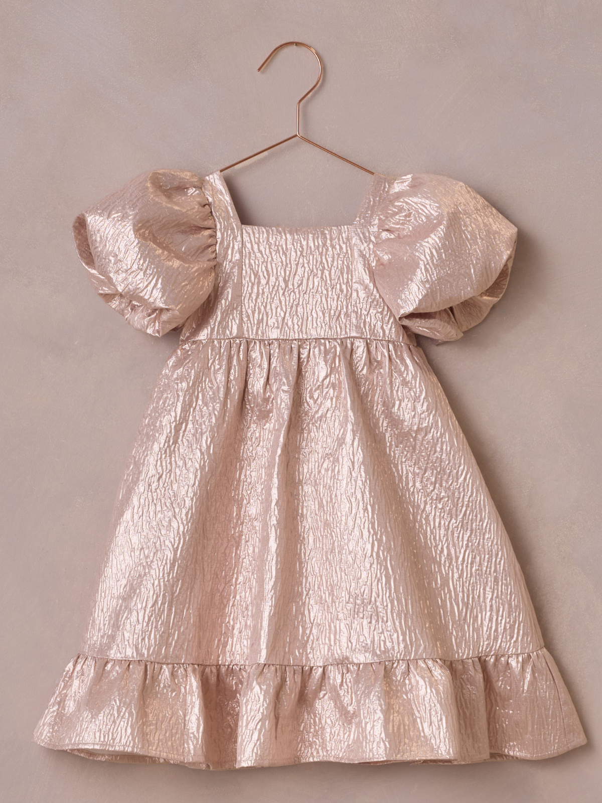 Pale pink dress with puff sleeves, hanging on a rose gold hook against a textured beige background.