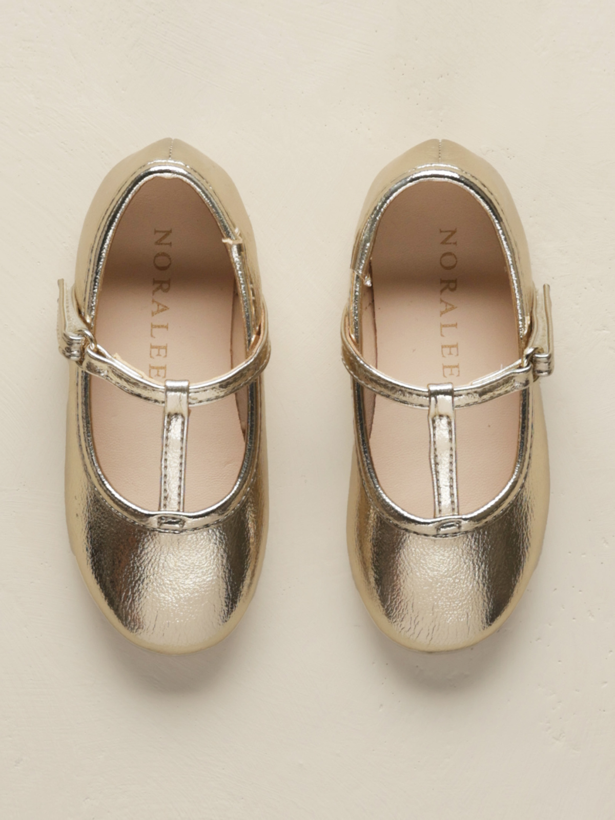 Gold metallic ballet shoes with a strap, top view on a light background.