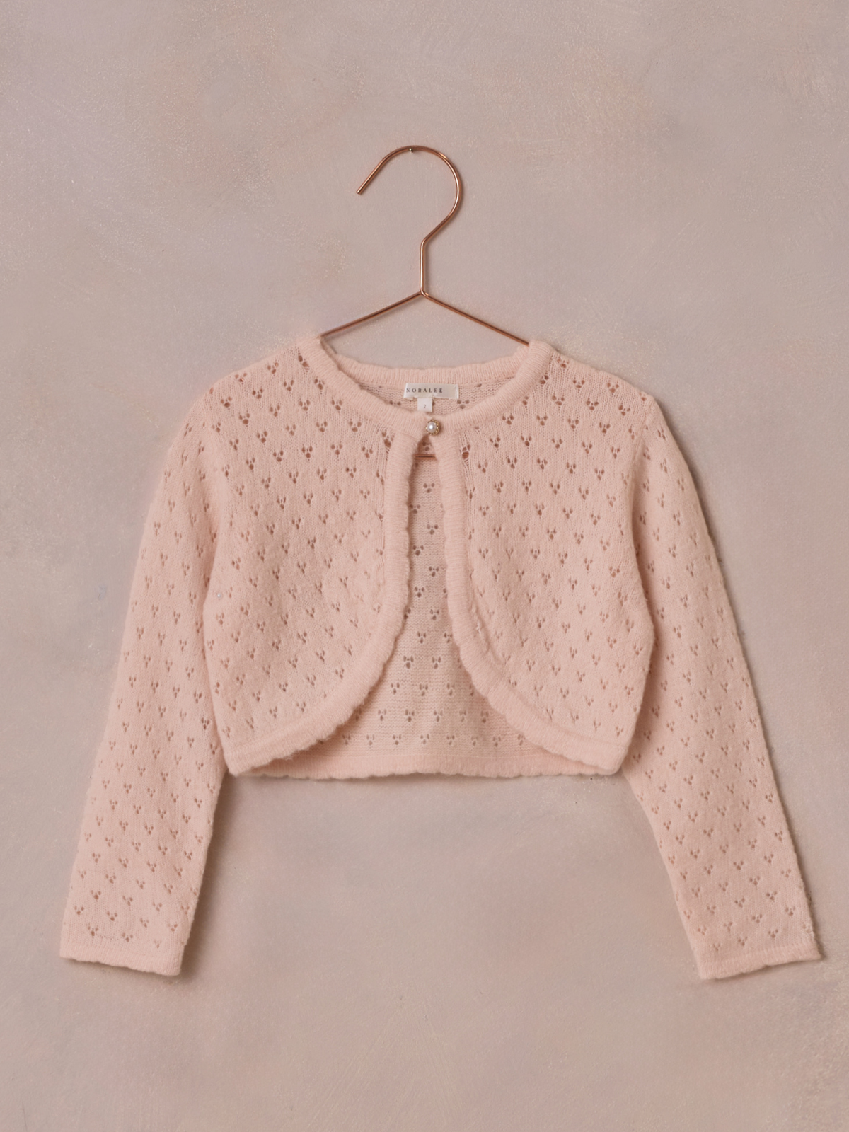Light pink knitted cardigan with a round neckline and button detail, hanging against a soft background.