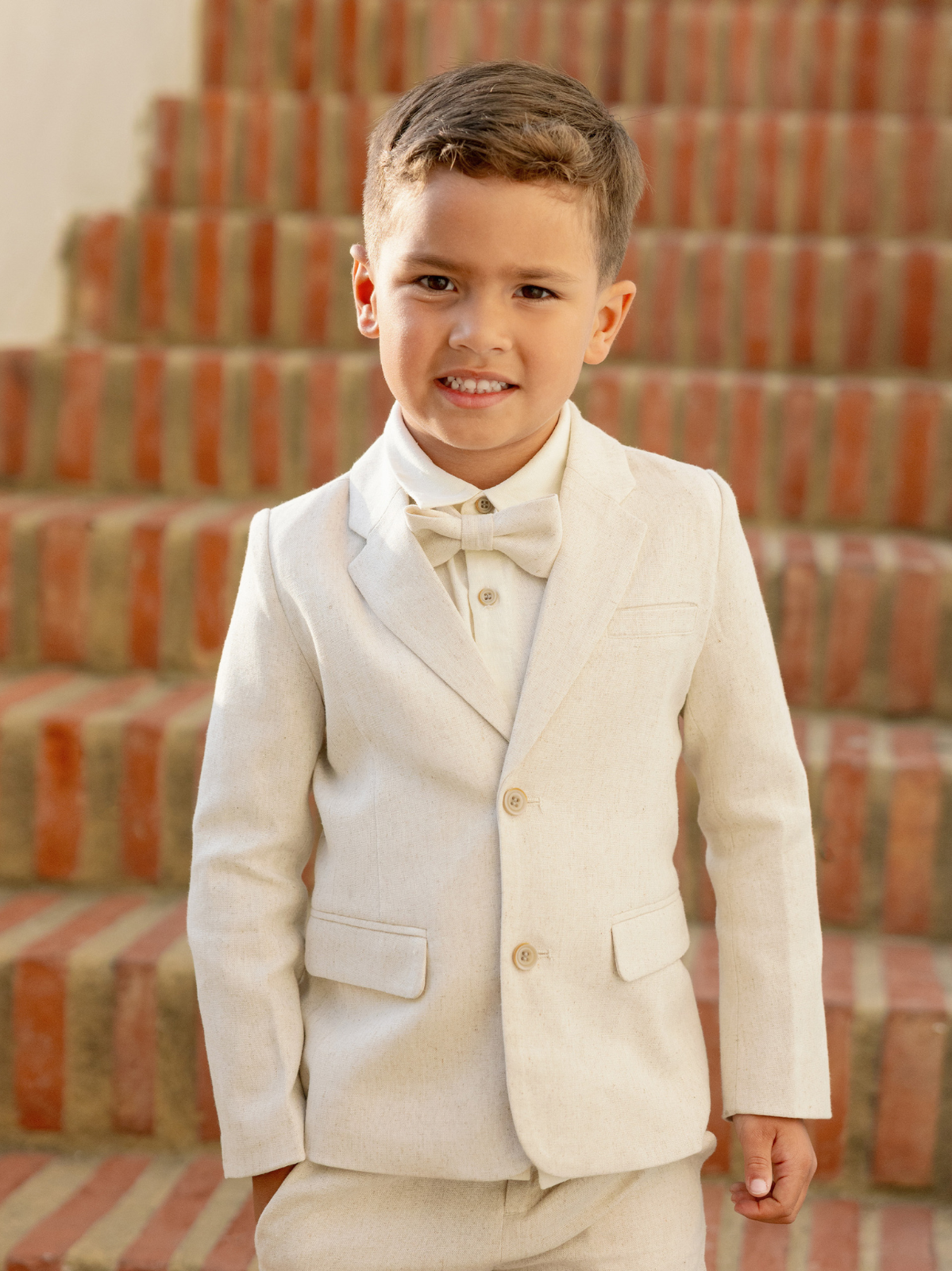 Smiling boy in a light suit stands on outdoor steps, looking at the camera with confidence.