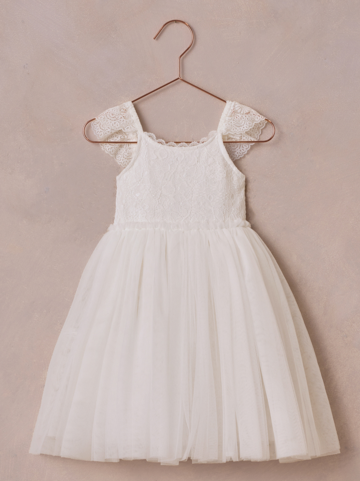 White lace dress with tulle skirt hanging on a rose gold hook against a soft, textured background.