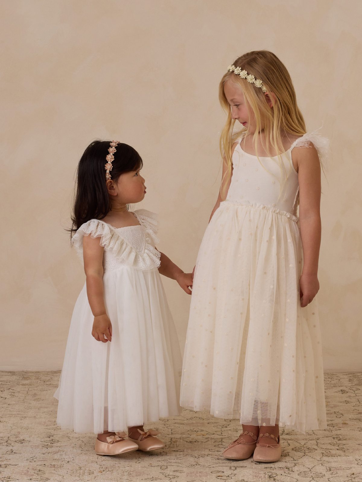 Two young girls in elegant white dresses stand side by side, sharing a joyful moment.