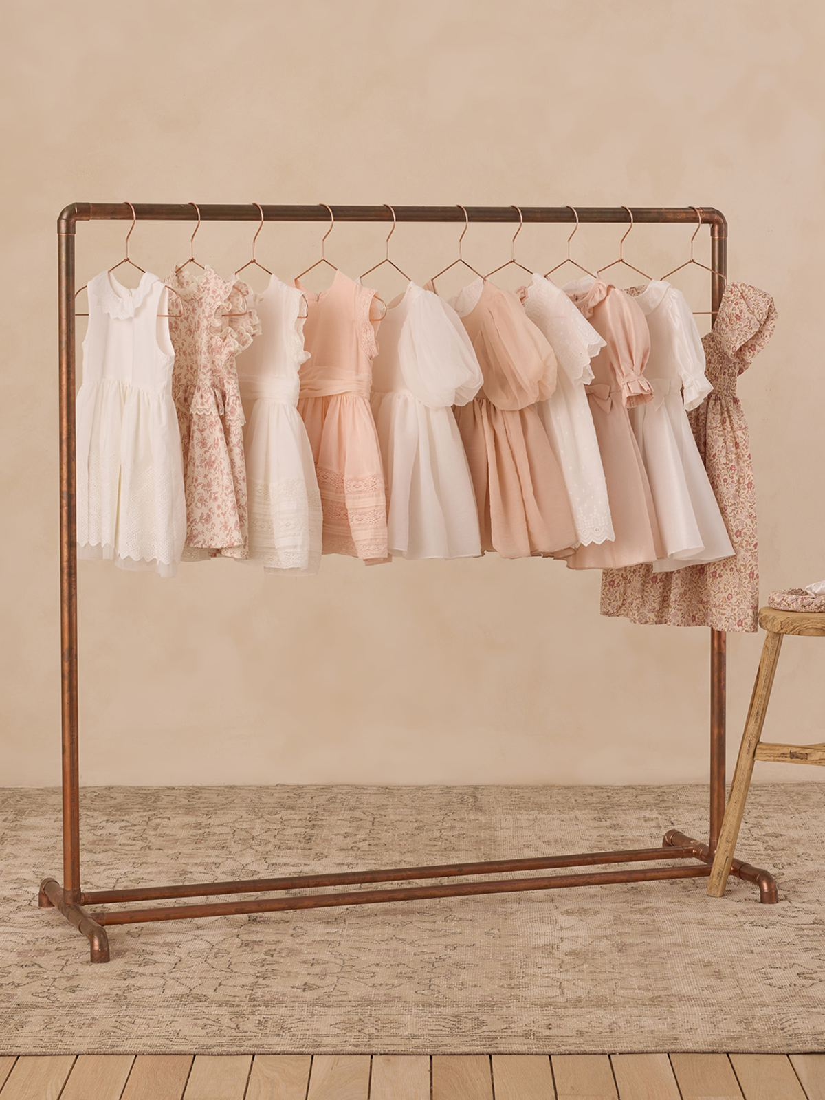 A rack displays a variety of children's dresses in soft pastel colors against a neutral backdrop.