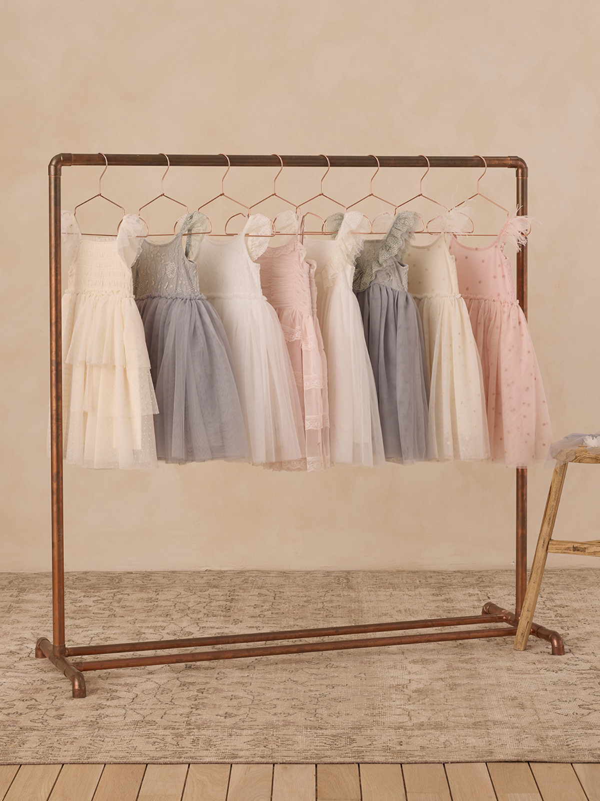 A clothing rack displaying pastel dresses in various styles and lengths, set against a beige background.