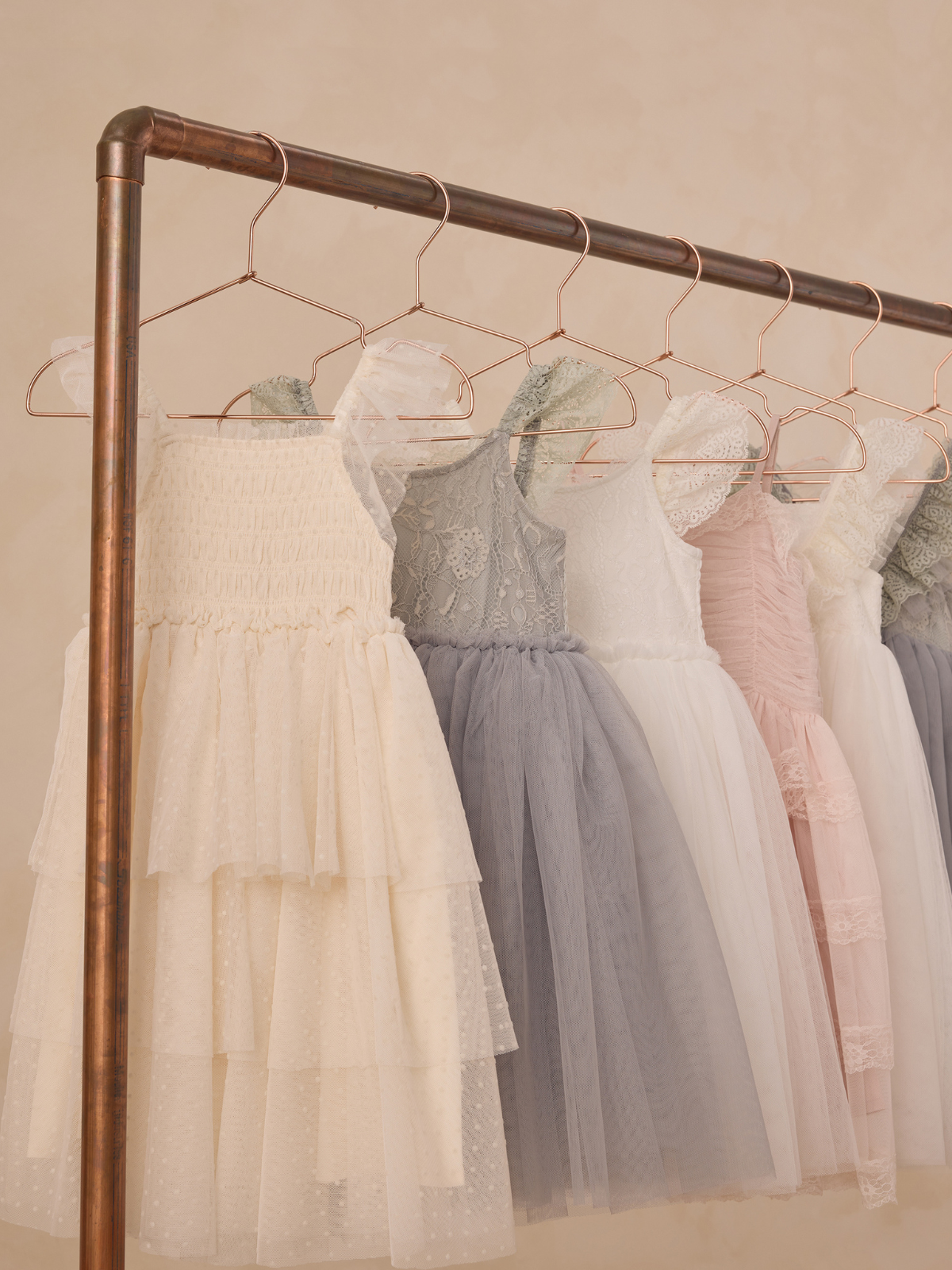 A rack displays various elegant tulle dresses in soft colors: white, gray, and pink.
