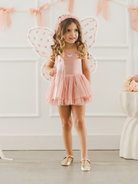 Girl in a pink fairy costume with wings, holding a wand, standing in a decorated room.