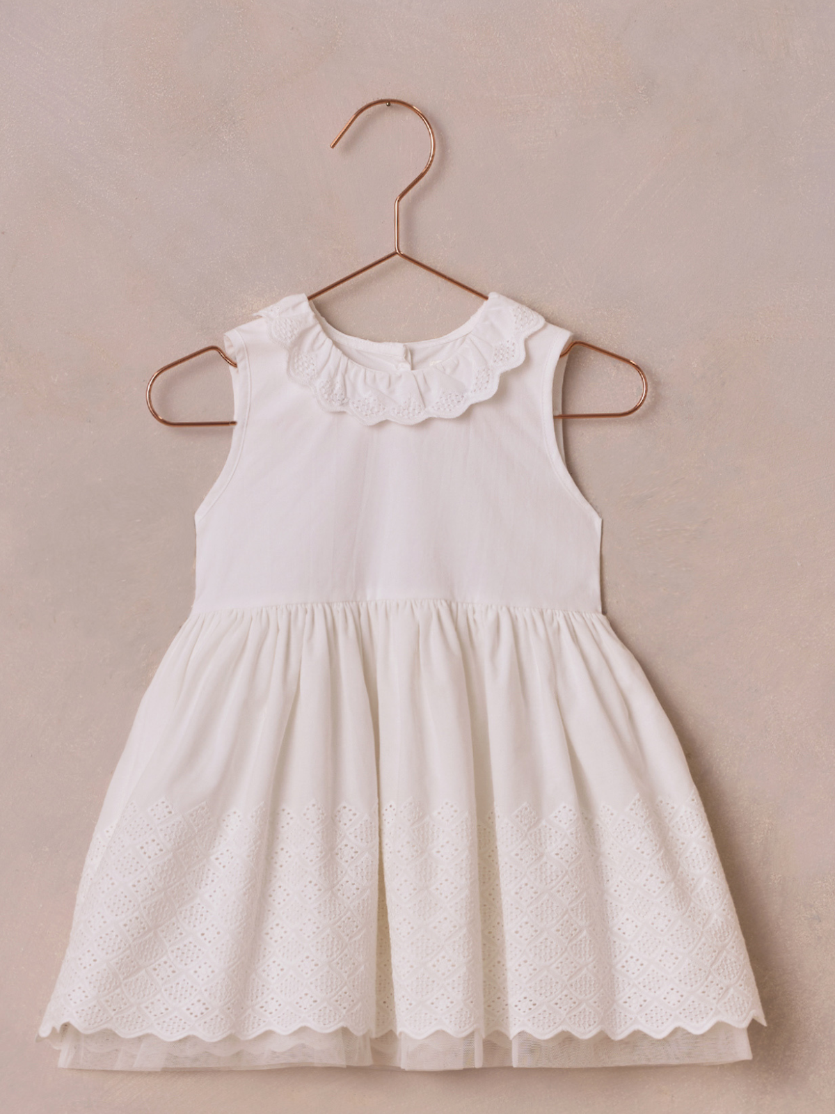 White sleeveless dress with a ruffled collar, hanging on a copper-colored hanger against a neutral background.