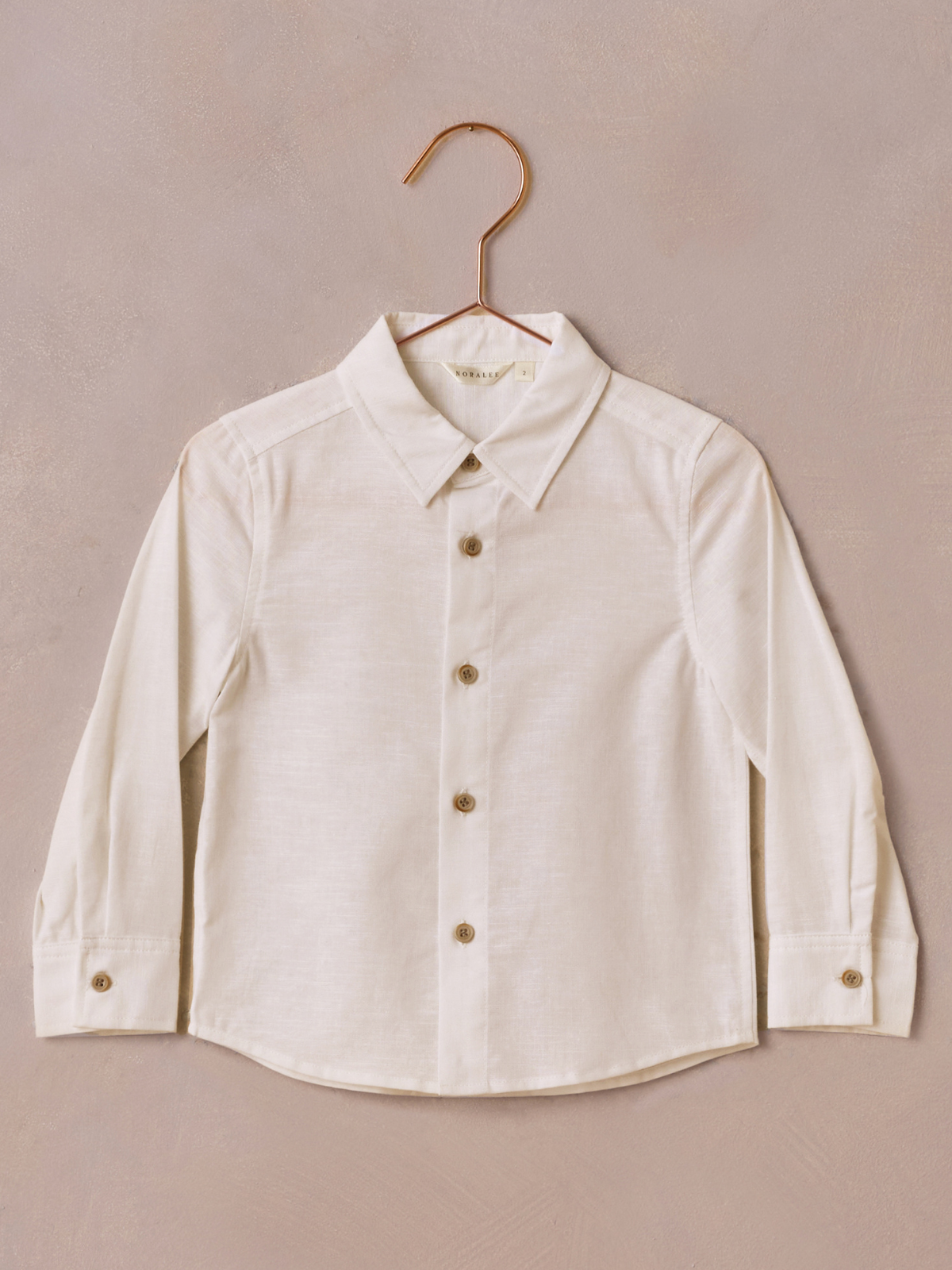 White long-sleeve button-up shirt on a rose gold hanger against a textured background.