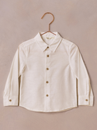 White long-sleeve button-up shirt on a rose gold hanger against a textured background.