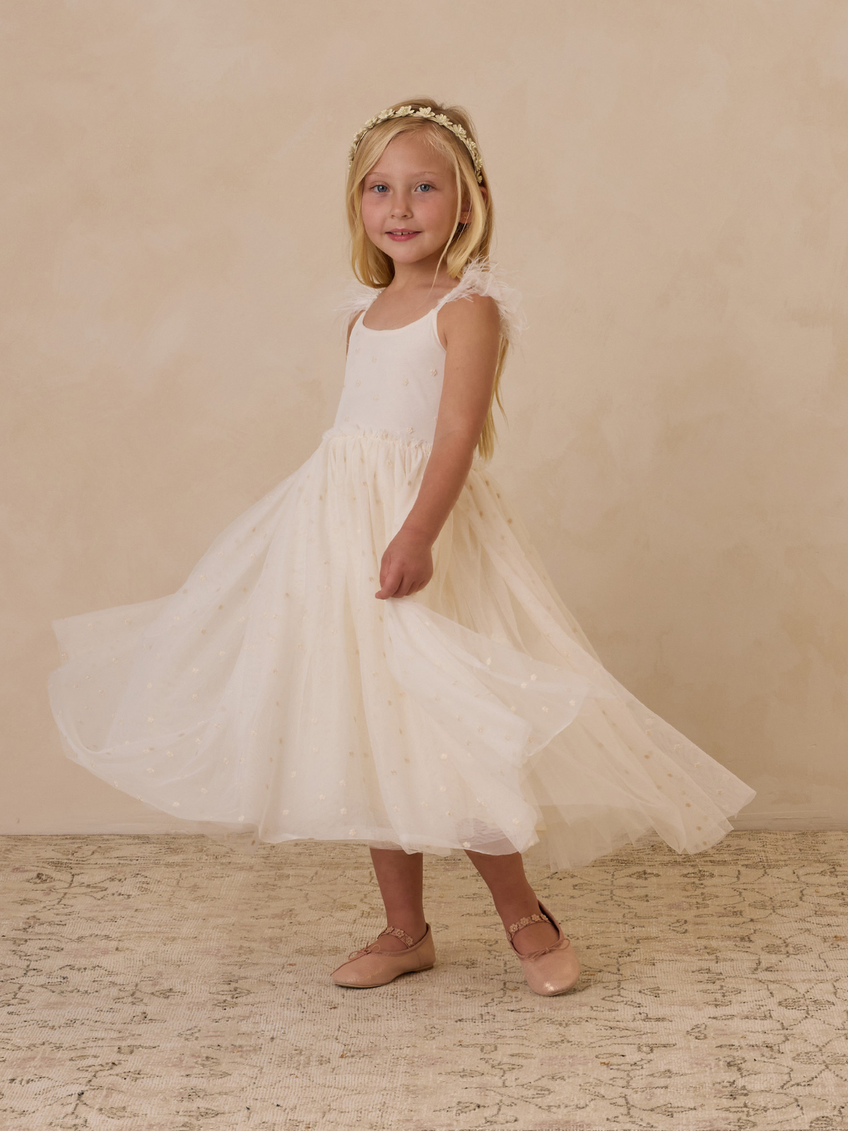 Young girl in a white dress twirling, wearing a floral headband, against a neutral background.