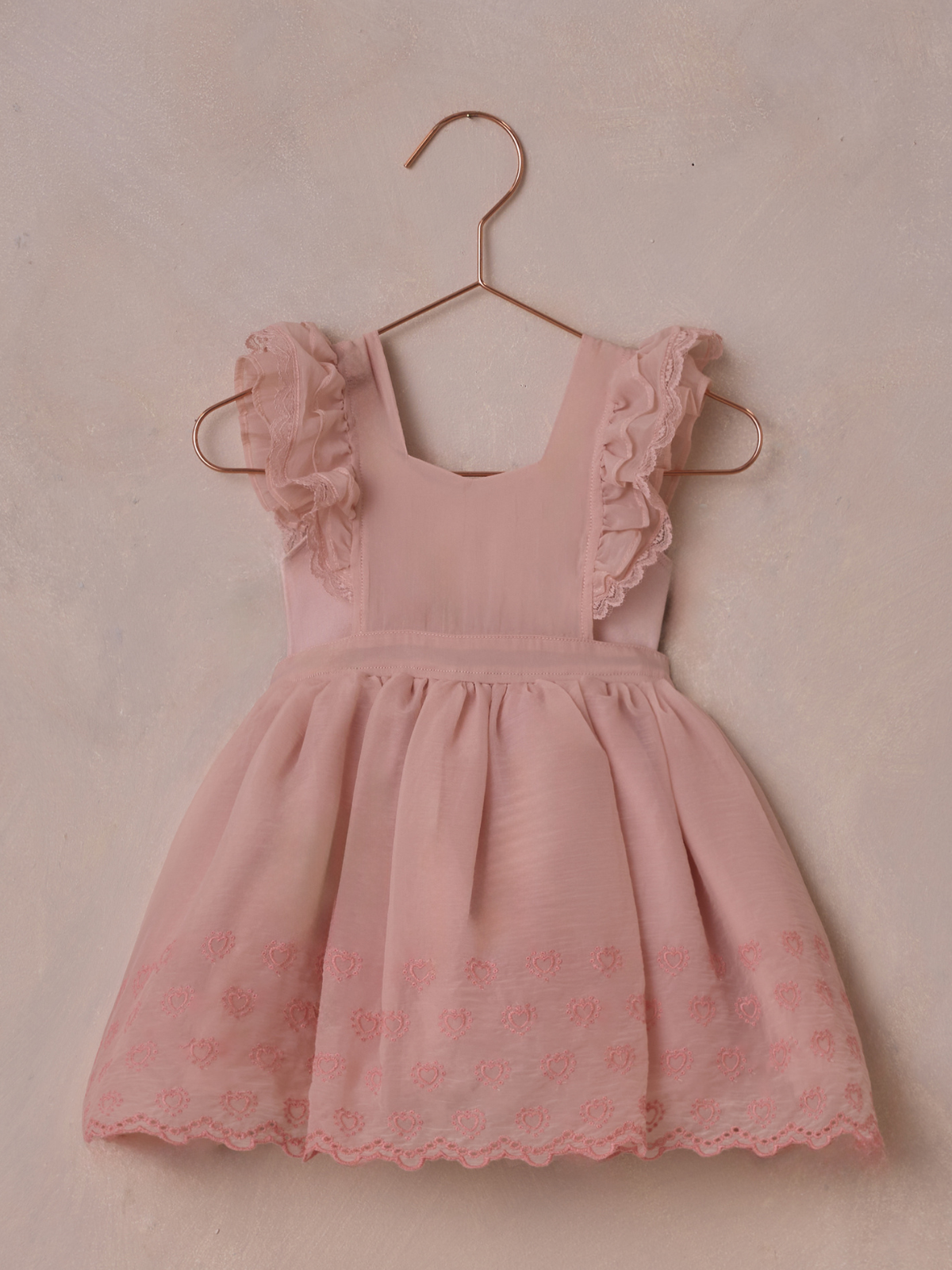 Pink toddler dress with ruffled sleeves hanging on a copper hanger against a soft, textured background.
