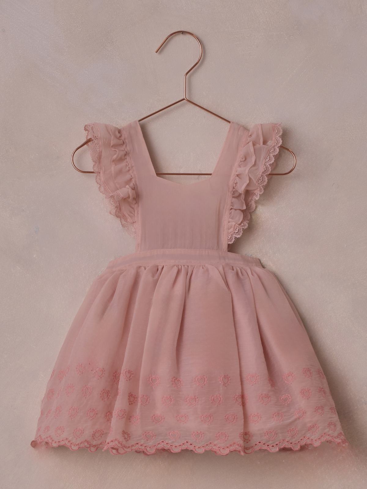 Pink dress with ruffled sleeves and heart embroidery, hanging on a copper hanger against a soft background.