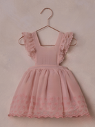 Pink dress with ruffled sleeves and heart embroidery, hanging on a copper hanger against a soft background.