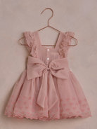 Pink dress with lace trim and bow, hanging on a rose gold hook against a soft background.