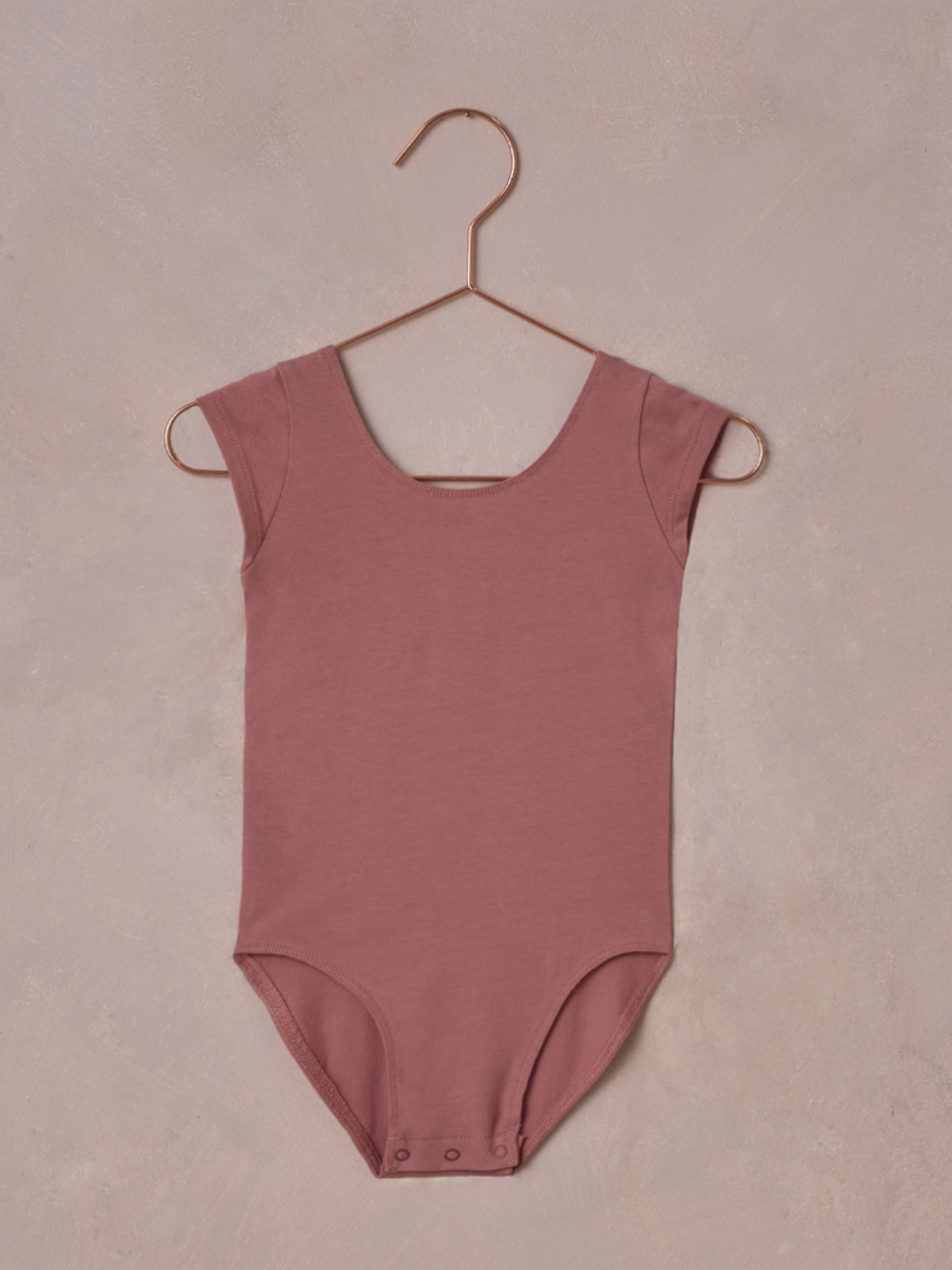 Light pink bodysuit hanging on a copper hook against a textured background.