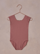 Light pink bodysuit hanging on a copper hook against a textured background.
