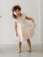 Young girl in a floral dress and pink headband, striking a playful pose on a light-colored background.