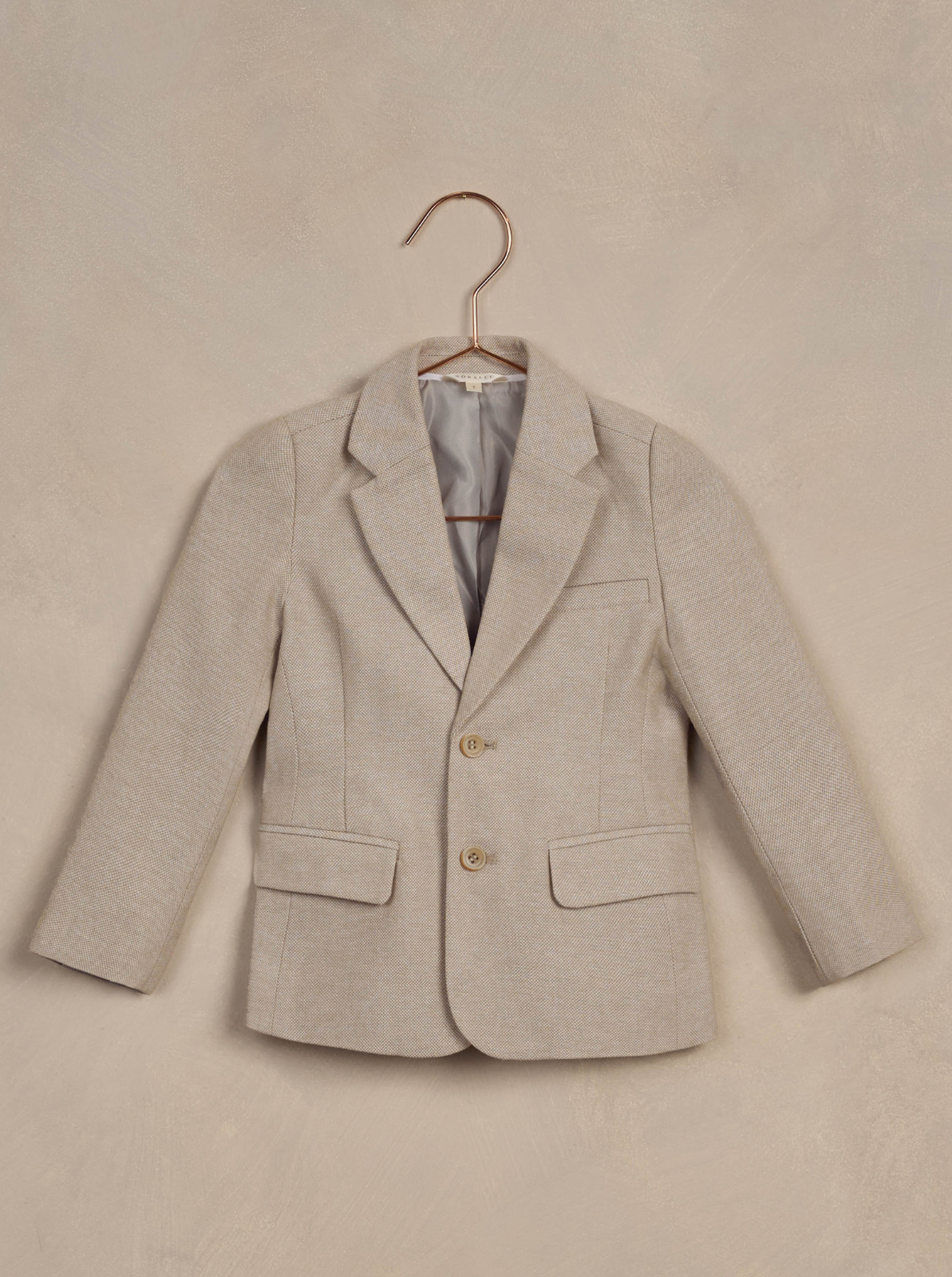 Light beige children's blazer displayed on a copper hanger against a neutral background.