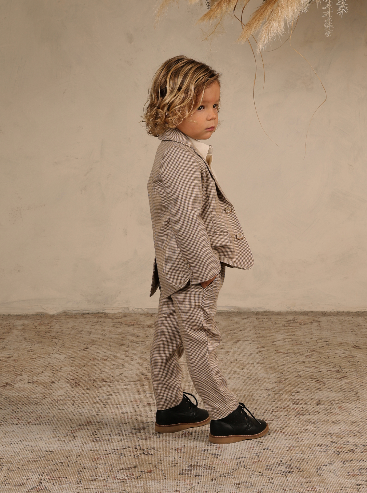 Child in a stylish beige suit stands confidently against a textured background. Perfect for formal occasions.