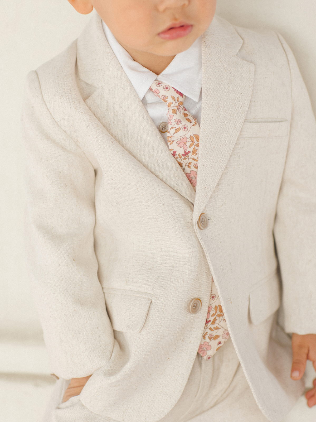Child in a light beige suit with a floral tie, posing against a plain background.