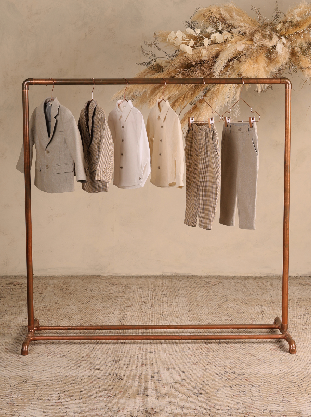 Children's clothing displayed on a copper rack against a textured background.