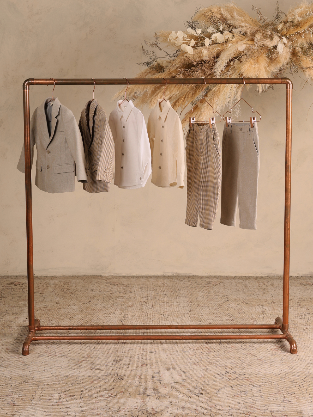 Display of children's formal wear, including blazers, shirts, and trousers, hanging on a copper rack.