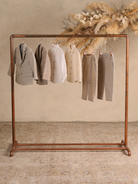 Display of children's formal wear, including blazers, shirts, and trousers, hanging on a copper rack.