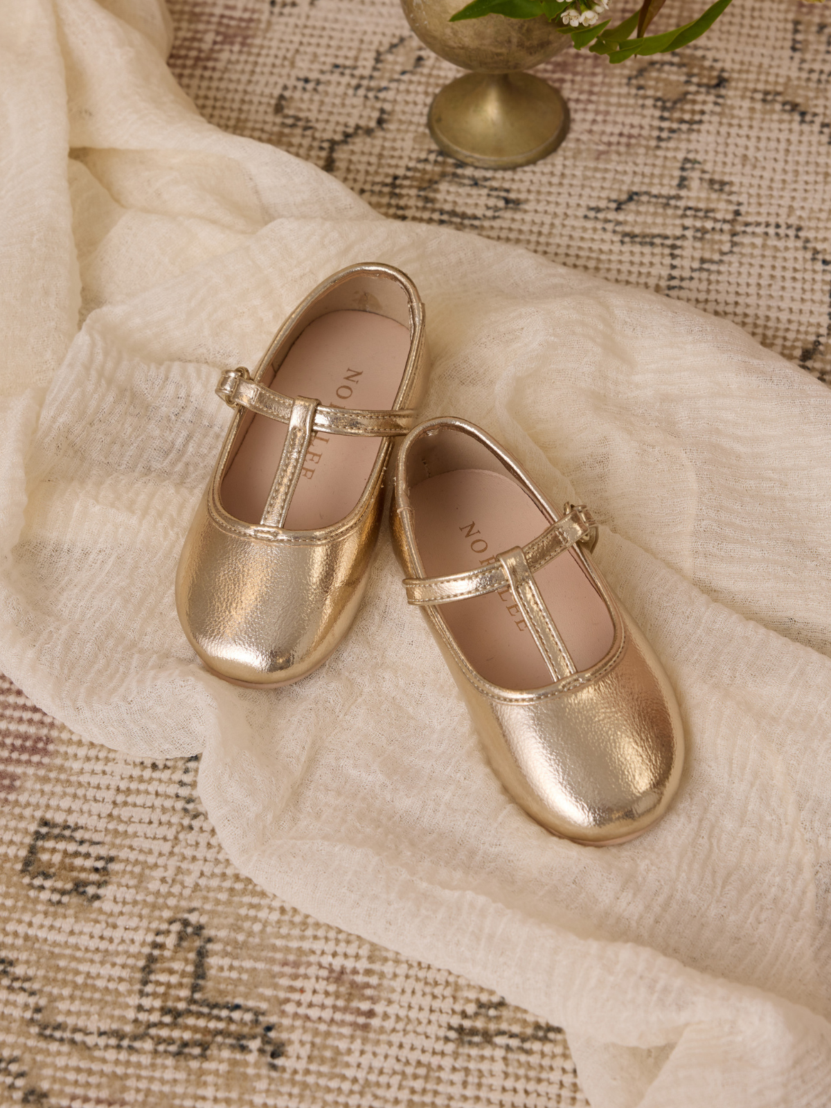 Gold children's Mary Jane shoes on a textured fabric background, showcasing their stylish design and soft shine.