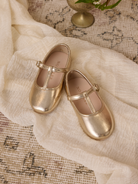 Gold children's Mary Jane shoes on a textured fabric background, showcasing their stylish design and soft shine.