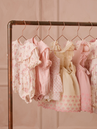 Stylish pink children's dresses hanging on a copper rack against a soft pink background.