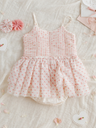Pink and white toddler dress with heart patterns, surrounded by fabric flowers and decorative accents on a soft background.