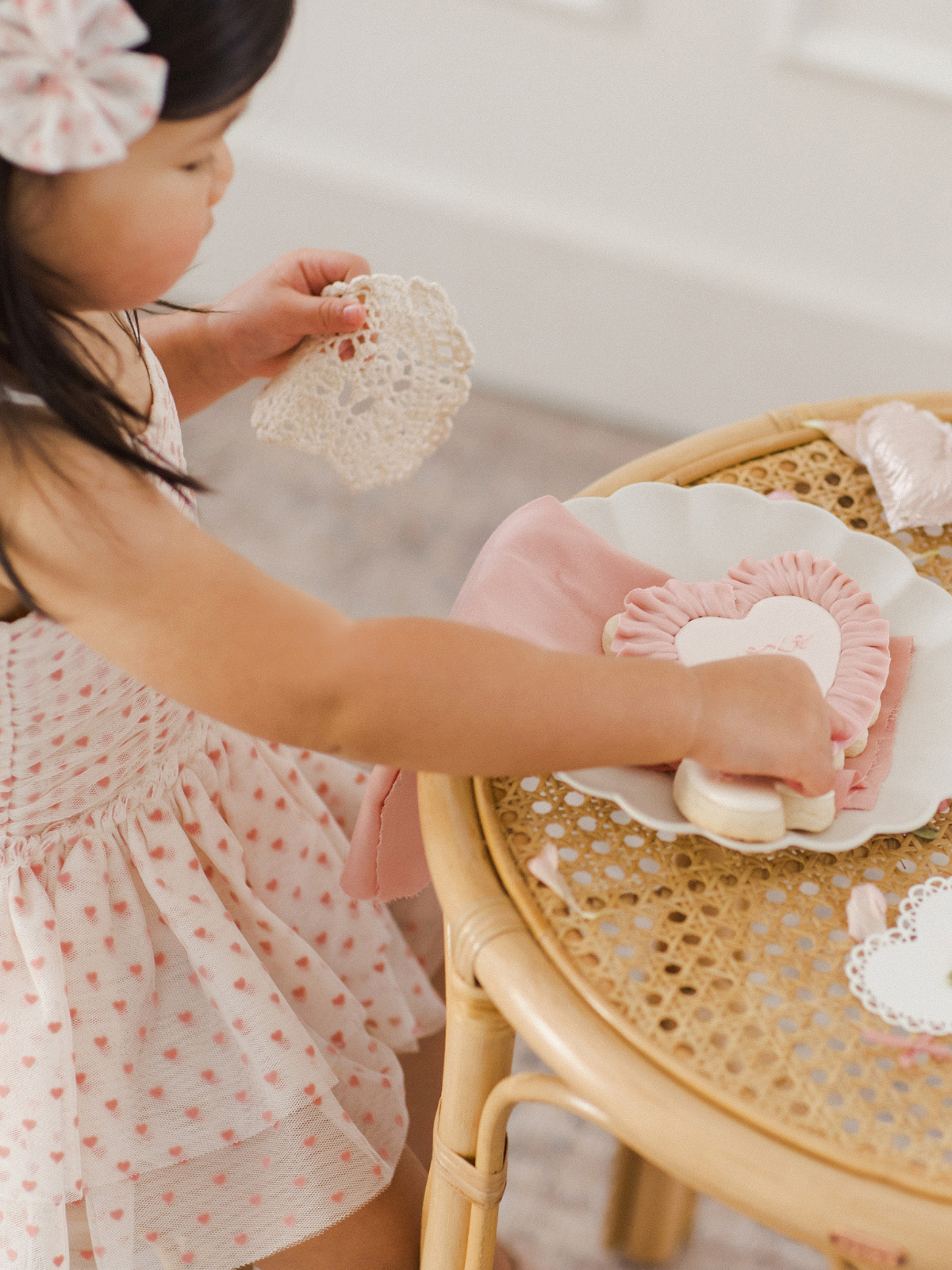 Young child arranging cookies on a decorative plate at a table, with a lace doily in hand.