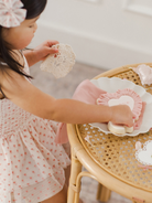 Young child arranging cookies on a decorative plate at a table, with a lace doily in hand.