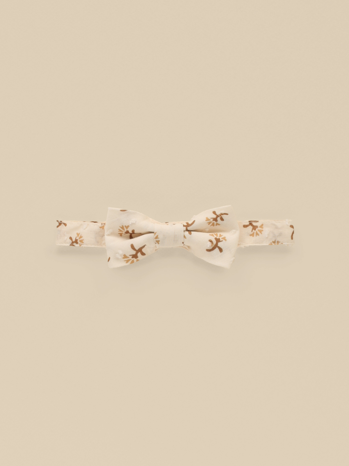 Cream bow tie with brown floral pattern on a beige background.
