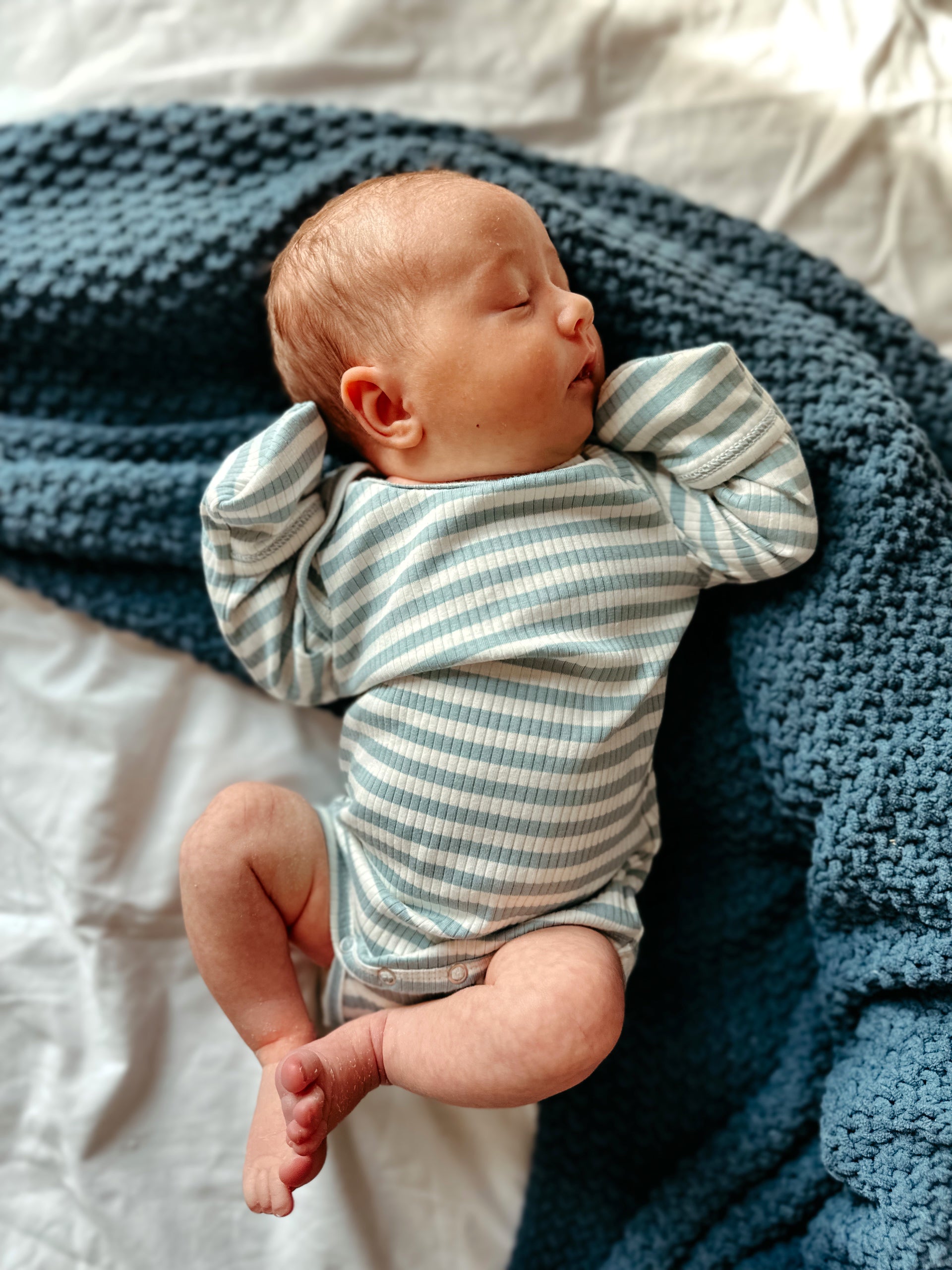 Sleeping newborn in a striped onesie, resting on a blue textured blanket.